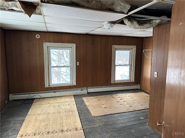 interior space featuring dark wood-style floors, a baseboard heating unit, wood walls, and a paneled ceiling