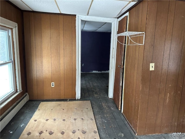 hall with wood walls, baseboard heating, dark wood finished floors, and a paneled ceiling