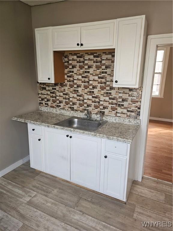 kitchen with light wood-type flooring, tasteful backsplash, white cabinets, and a sink