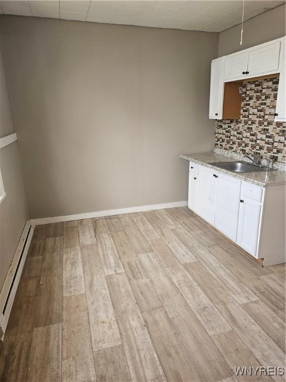 kitchen featuring white cabinets, light stone counters, baseboard heating, light wood-type flooring, and backsplash