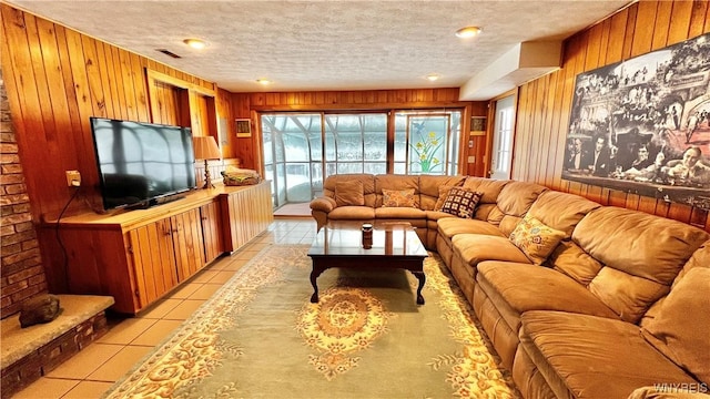 living room with wooden walls, visible vents, light tile patterned flooring, and a textured ceiling