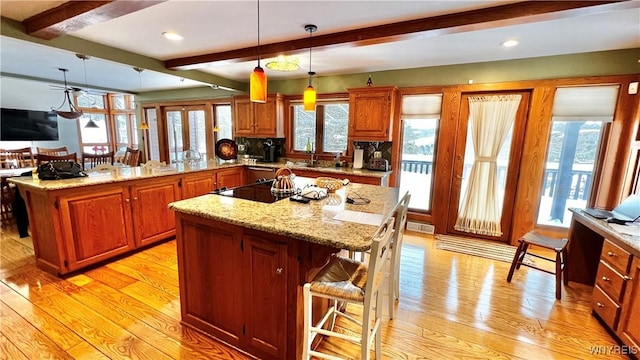 kitchen featuring a kitchen island, a breakfast bar, beamed ceiling, a peninsula, and light wood-type flooring