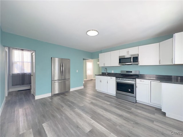 kitchen with baseboards, dark countertops, appliances with stainless steel finishes, light wood-type flooring, and white cabinetry