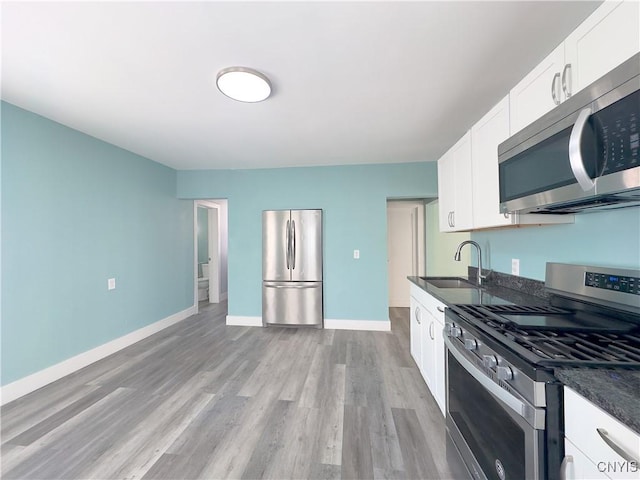 kitchen with light wood-style flooring, a sink, white cabinets, appliances with stainless steel finishes, and dark countertops