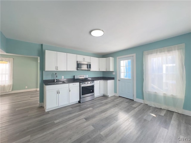 kitchen featuring dark countertops, appliances with stainless steel finishes, white cabinets, a sink, and baseboards