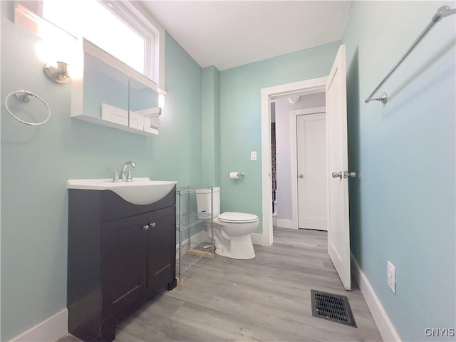 half bathroom with toilet, wood finished floors, vanity, visible vents, and baseboards