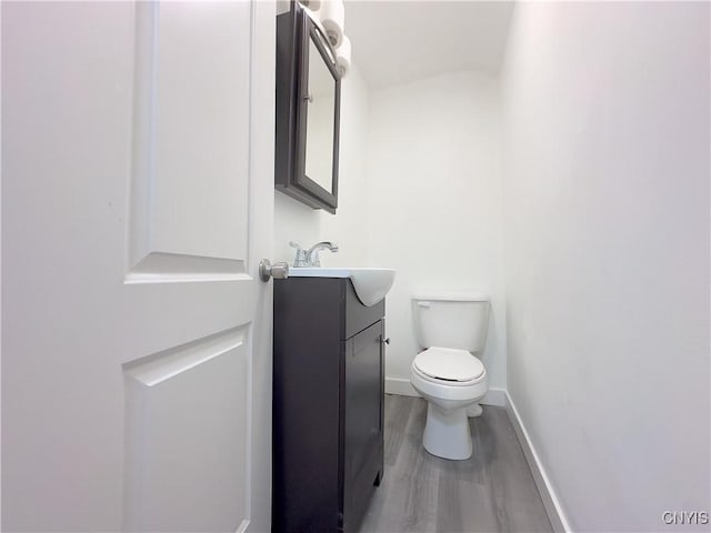 half bathroom featuring toilet, baseboards, wood finished floors, and vanity