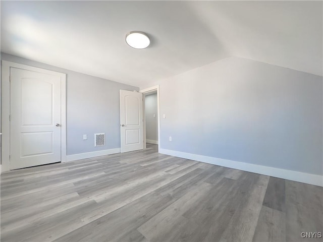 interior space featuring light wood-style flooring, visible vents, vaulted ceiling, and baseboards