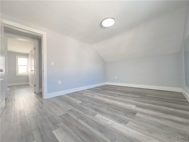 bonus room with light wood-type flooring, vaulted ceiling, and baseboards