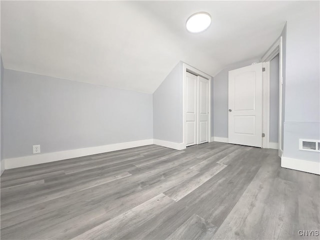 additional living space with visible vents, vaulted ceiling, baseboards, and wood finished floors