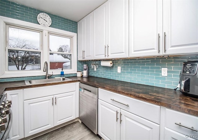 kitchen with dishwasher, dark countertops, a sink, and white cabinetry