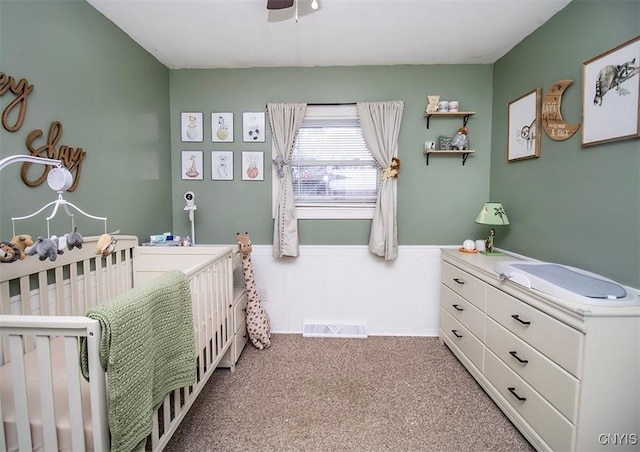 bedroom featuring visible vents, a ceiling fan, wainscoting, carpet, and a nursery area