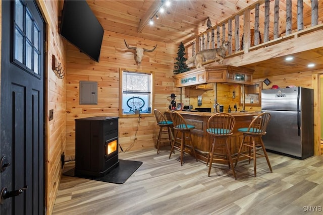 bar with electric panel, freestanding refrigerator, a wood stove, wood walls, and light wood-style floors