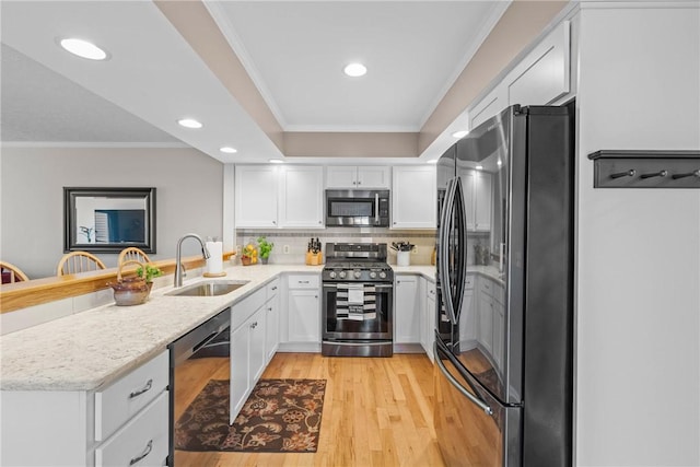 kitchen featuring ornamental molding, stainless steel appliances, light wood-style floors, white cabinetry, and a sink