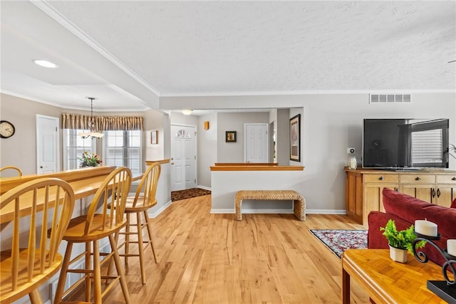 living room featuring light wood-style floors, visible vents, and crown molding