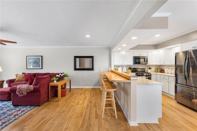 kitchen featuring appliances with stainless steel finishes, open floor plan, white cabinets, a peninsula, and a kitchen bar