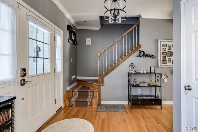 foyer entrance featuring a chandelier, light wood finished floors, stairway, and crown molding