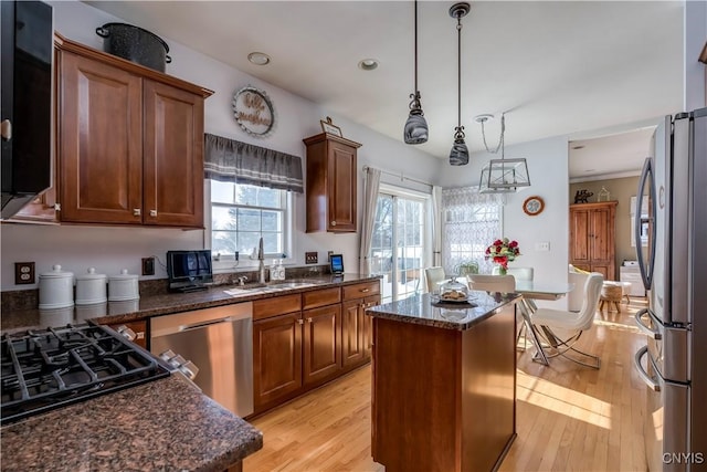 kitchen with light wood-style flooring, appliances with stainless steel finishes, a center island, hanging light fixtures, and a sink