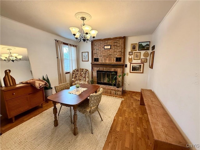 dining area with an inviting chandelier, a brick fireplace, and wood finished floors