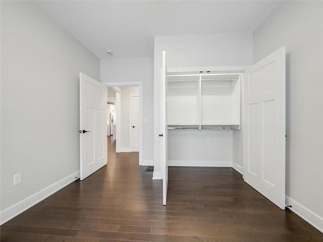 unfurnished bedroom with dark wood-type flooring, a closet, and baseboards