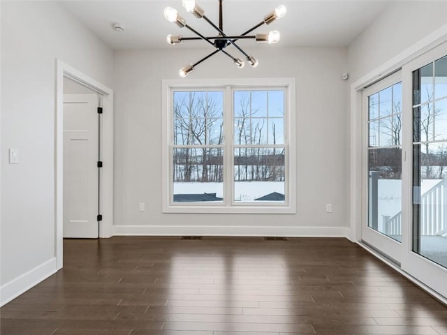 unfurnished dining area featuring dark wood-type flooring, a wealth of natural light, baseboards, and an inviting chandelier