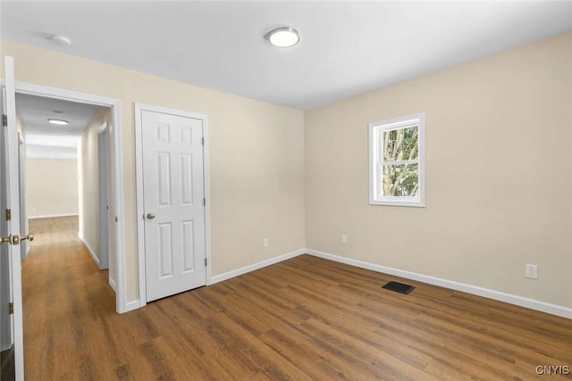 empty room with dark wood finished floors, visible vents, and baseboards