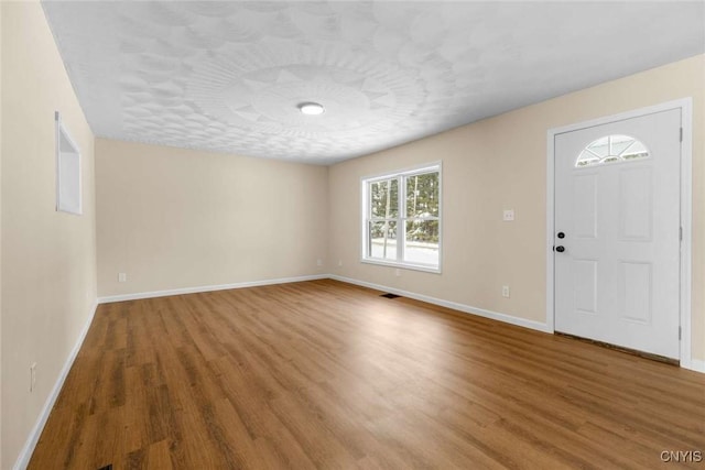 foyer entrance with a textured ceiling, baseboards, and wood finished floors