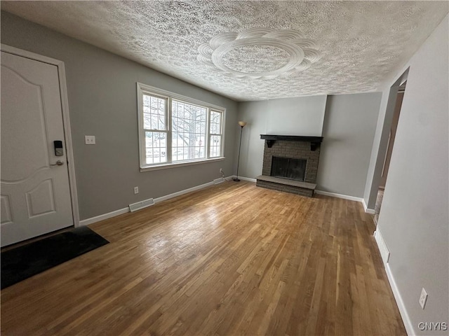 unfurnished living room featuring a brick fireplace, a textured ceiling, baseboards, and wood finished floors