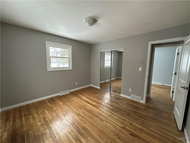 unfurnished bedroom with a closet, wood finished floors, visible vents, and baseboards