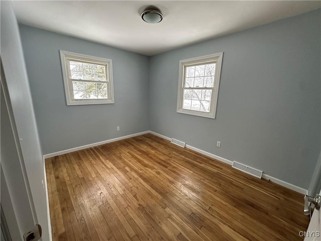 empty room with baseboards, visible vents, and wood finished floors