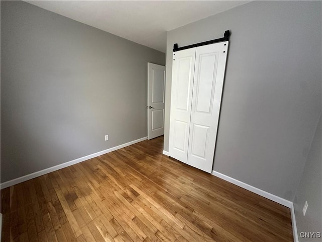 unfurnished bedroom with a barn door, wood finished floors, and baseboards