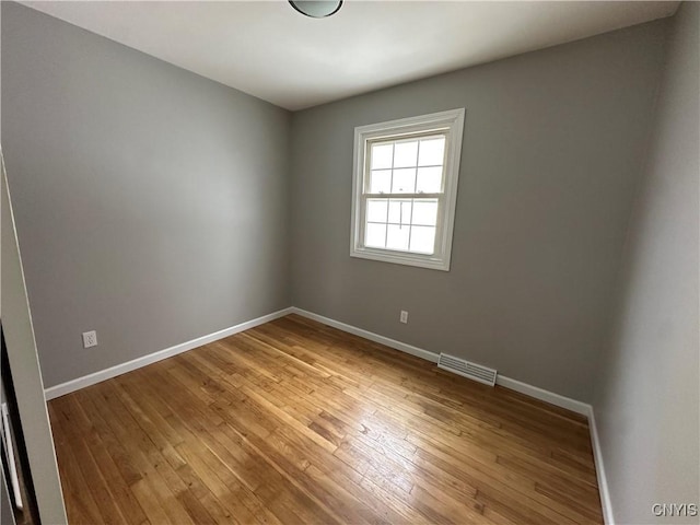 unfurnished room with wood finished floors, visible vents, and baseboards