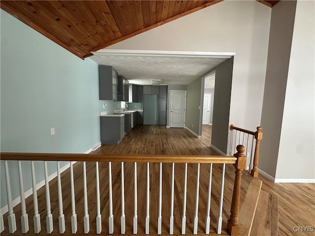 corridor featuring wooden ceiling, a sink, baseboards, vaulted ceiling, and light wood-type flooring