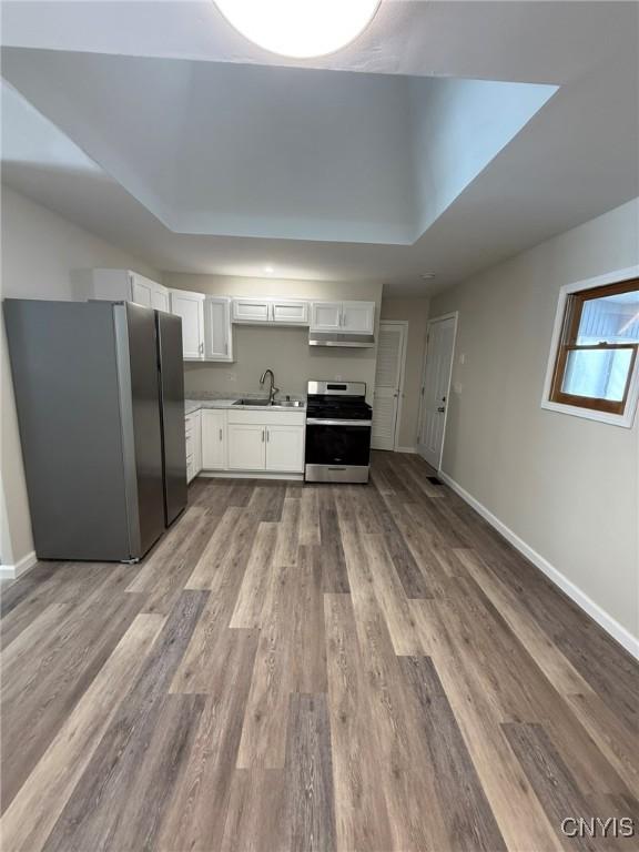 kitchen featuring light wood-style flooring, stainless steel appliances, a sink, baseboards, and white cabinets