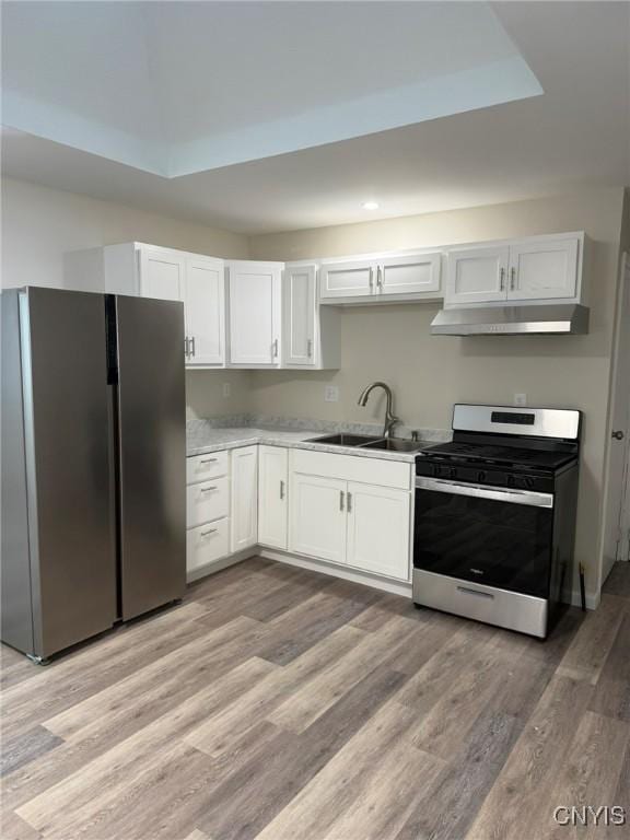 kitchen with light wood finished floors, appliances with stainless steel finishes, under cabinet range hood, white cabinetry, and a sink