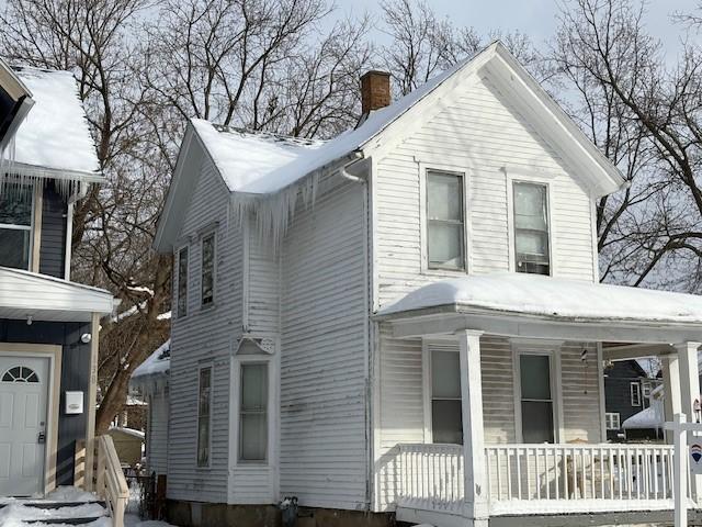 snow covered property with covered porch and a chimney