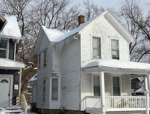 snow covered property featuring a porch and a chimney