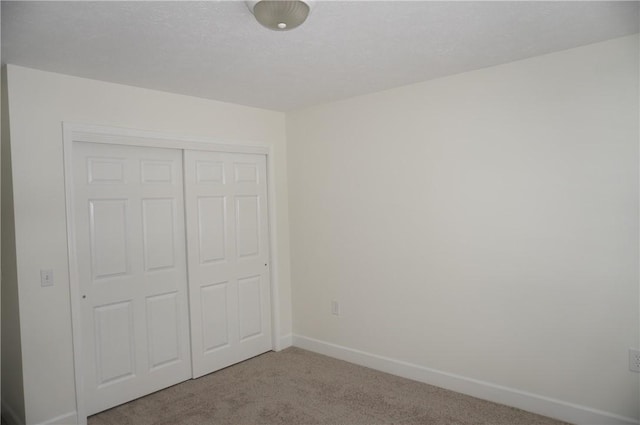 unfurnished bedroom featuring light carpet, a textured ceiling, baseboards, and a closet