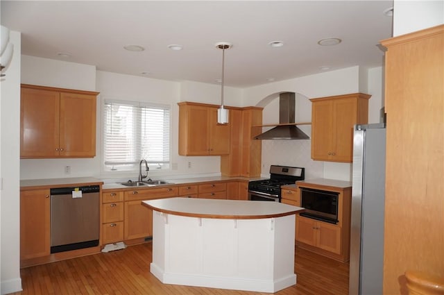 kitchen with appliances with stainless steel finishes, decorative light fixtures, light countertops, wall chimney range hood, and a sink