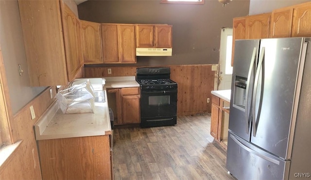 kitchen with stainless steel refrigerator with ice dispenser, light countertops, black gas range oven, wood finished floors, and under cabinet range hood