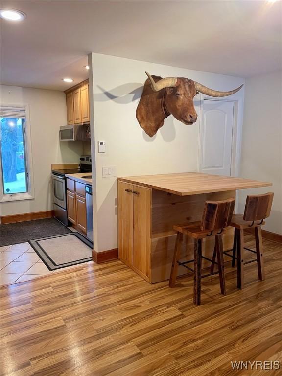 bar with stainless steel appliances, light wood-type flooring, and baseboards