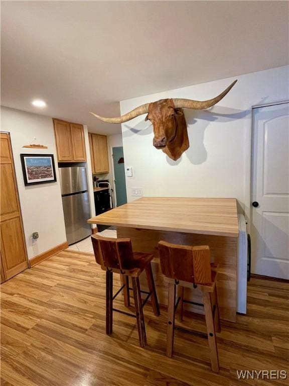 kitchen with recessed lighting, a kitchen breakfast bar, baseboards, light wood-style floors, and freestanding refrigerator