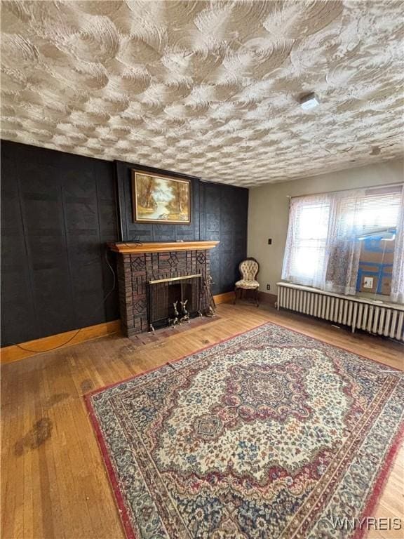 interior space with baseboards, radiator, a fireplace with flush hearth, wood finished floors, and a textured ceiling