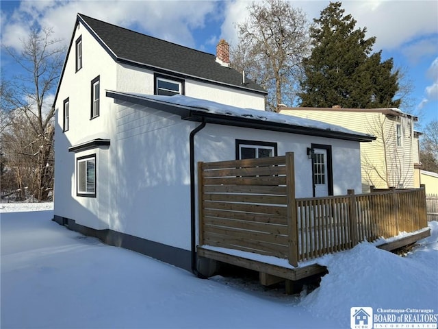 snow covered rear of property with a chimney and stucco siding