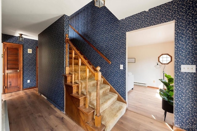 stairs featuring a baseboard heating unit, wood finished floors, baseboards, and wallpapered walls