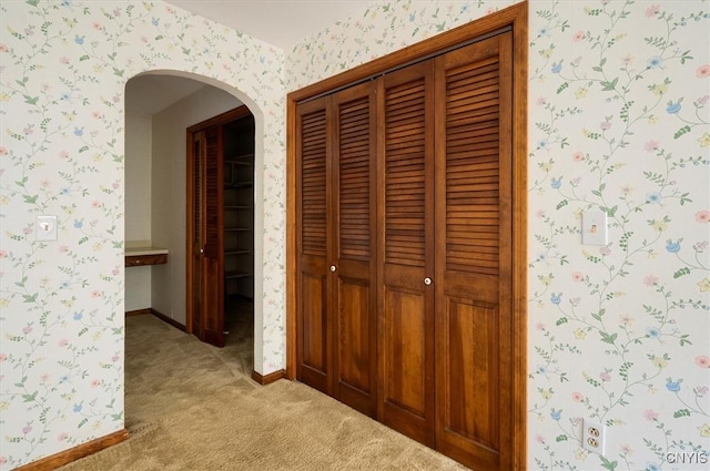 hallway with baseboards, light colored carpet, and wallpapered walls