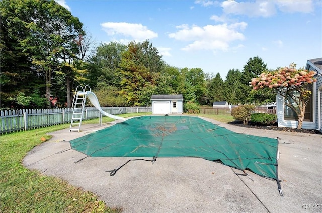 view of pool featuring an outbuilding, a water slide, a fenced backyard, a fenced in pool, and a shed