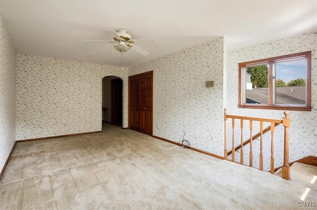 unfurnished room featuring light carpet, wallpapered walls, baseboards, arched walkways, and ceiling fan