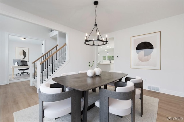 dining area featuring stairway, a notable chandelier, visible vents, and wood finished floors