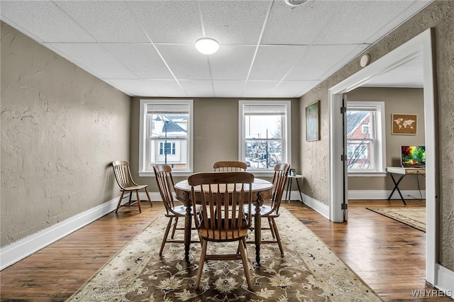 dining area with a paneled ceiling, wood finished floors, and a textured wall